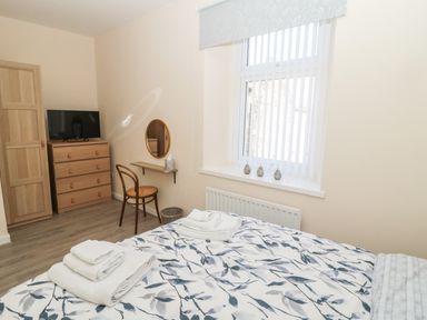 A bedroom with a bed with folded towels a wooden chair a chest of drawers with a television and a window with vertical blinds at Stones Throw in Amble