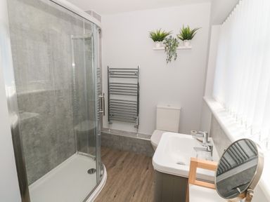 A bathroom with a shower enclosure a toilet a sink and a round mirror at Stones Throw in Amble