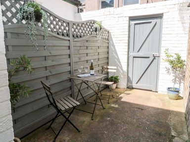 A small outdoor patio with a wooden table and two chairs near a gray wooden fence and a gray door at Stone's Throw in Amble