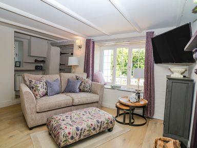 A sitting room with a beige sofa purple cushions floral patterned ottoman wooden nesting tables lamp and wall mounted tv at Hillside in Crafthole