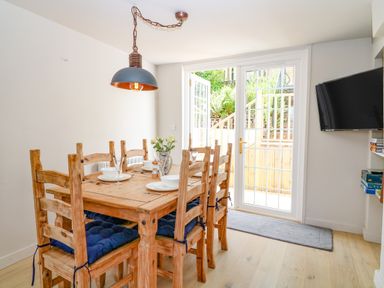 A dining room with a wooden table and six chairs near glass doors leading outside at Hillside in Crafthole