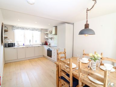 A kitchen with white cabinets and a wooden dining table with chairs at Hillside in Crafthole