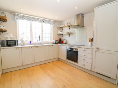 A kitchen with white cabinets wooden shelves and appliances including a microwave toaster and stove at Hillside in Crafthole