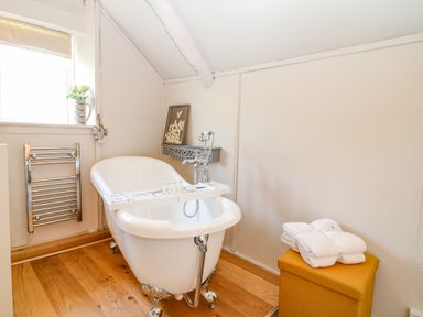 A bathroom with a clawfoot bathtub a small shelf with decorations a window with flowers and a wall-mounted towel warmer at Hillside in Crafthole