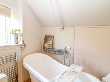 A bathroom with a white freestanding bathtub a window with flowers on the sill and a decorative wall shelf at Hillside in Crafthole