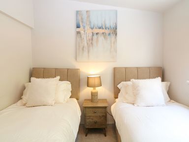 A bedroom with two single beds a bedside table with a lamp and a painting on the wall at Hillside in Crafthole