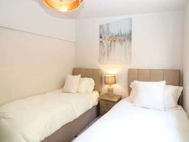 A bedroom with two single beds a nightstand with a lamp and a painting on the wall at Hillside in Crafthole
