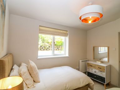A bedroom with a bed white bedding a window with a blind a lamp a dresser with a mirror and a ceiling light at Hillside in Crafthole