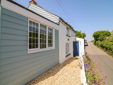 A house exterior with blue door gravel path white fence and flowers along a road at Hillside in Crafthole