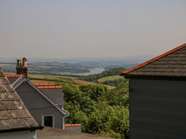 A landscape view with rooftops and chimneys in the foreground and fields trees and a river in the distance at Hillside in Crafthole