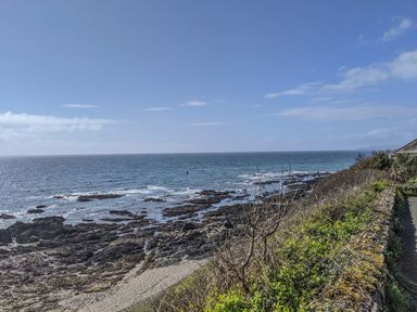 A rocky coastline with ocean waves and a stone wall with vegetation at Hillside in Crafthole