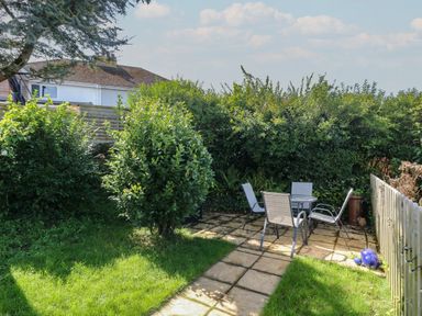 A garden with a paved seating area containing a table and four chairs surrounded by bushes and a wooden fence at Hillside in Crafthole