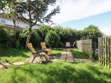 A garden with two yellow cushioned chairs and a table on a patio with grass and trees at Hillside in Crafthole