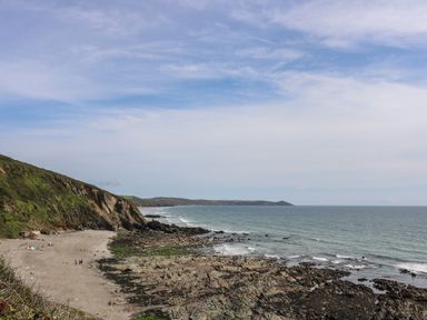 A rocky beach with people on the shore and cliffs on the left at Hillside in Crafthole