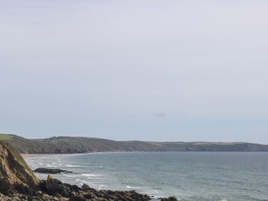 A coastal landscape with rocky shoreline and hills in the distance at Hillside in Crafthole