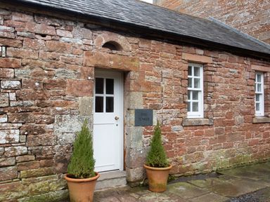 A stone building exterior with a white door two potted plants and two windows at The Tower in Kirklinton near Longtown