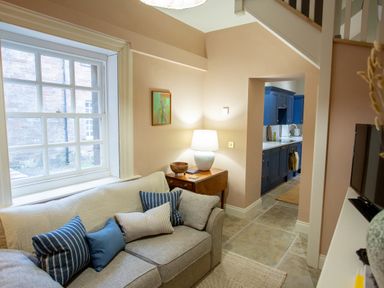 A living room with a gray sofa and blue cushions next to a window and a side table with a lamp and a wooden bowl at The Tower in Kirklinton near Longtown