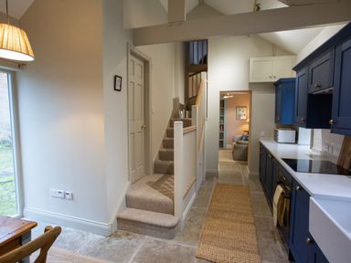 A kitchen with blue cabinets and a stove next to stairs and a hallway at The Tower in Kirklinton near Longtown