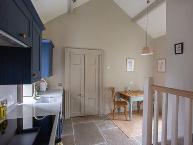 A kitchen with blue cabinets a wooden table and chairs and framed pictures on the wall at The Tower in Kirklinton near Longtown