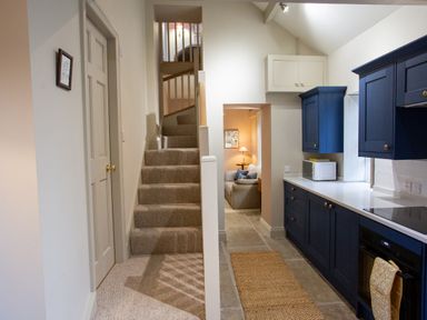 A kitchen with blue cabinets a staircase with carpet and a sitting area with a sofa and lamp at The Tower Kirklinton near Longtown