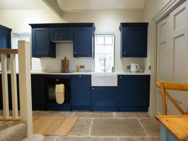 A kitchen with blue cabinets a white sink an oven and a wooden chair at The Tower Kirklinton near Longtown