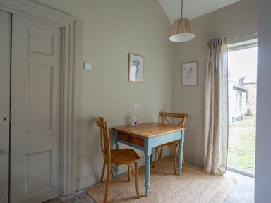 A small dining area with a wooden table and two chairs near a window with curtains at The Tower Kirklinton near Longtown