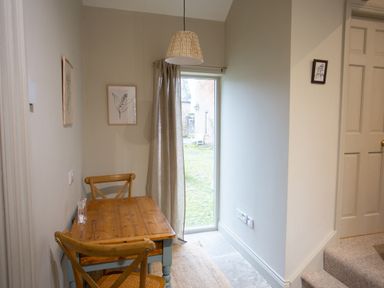A small dining area with a wooden table and two chairs next to a glass door with curtains at The Tower in Kirklinton near Longtown