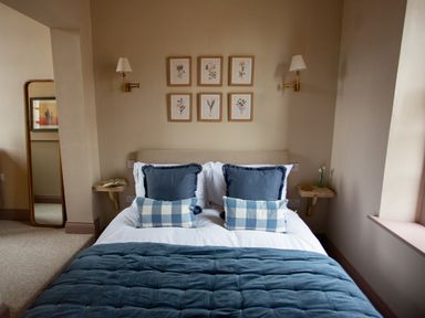 A bedroom with a bed with blue and white pillows blue quilt wall lamps and framed botanical prints at The Tower in Kirklinton near Longtown