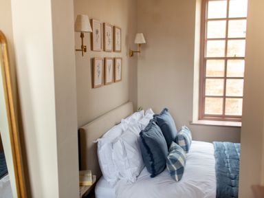 A bedroom with a bed with white and blue pillows next to a window with framed pictures and wall lamps at The Tower in Kirklinton near Longtown