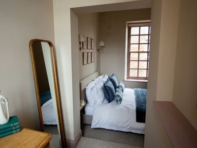 A bedroom with a bed and pillows next to a window and a standing mirror at The Tower in Kirklinton near Longtown