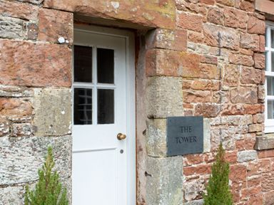 A white door with four glass panels set in a red stone wall with a sign saying The Tower at The Tower in Kirklinton near Longtown