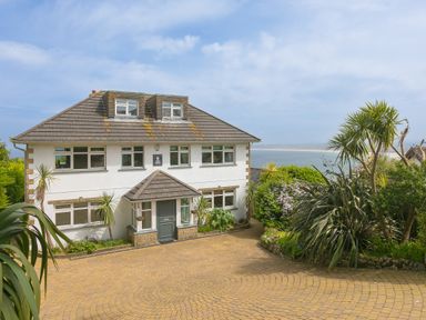 A two story house with multiple windows a gray roof and a paved driveway with plants and trees near the house at Moonbeams in Carbis Bay
