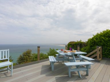 A deck with a picnic table and bench seating overlooking the ocean at Moonbeams in Carbis Bay