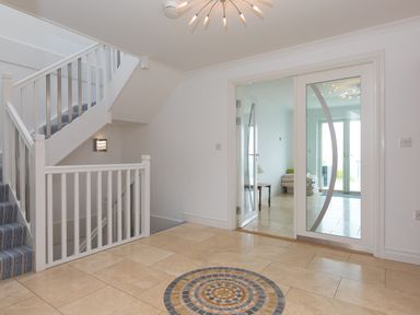 An entryway with tiled floor and circular mosaic design staircase with striped carpet and glass double doors leading to another room at Moonbeams in Carbis Bay