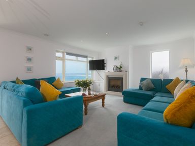 A living room with blue sofas and yellow cushions a wooden table with flowers and a fireplace with a TV on the wall at Moonbeams in Carbis Bay