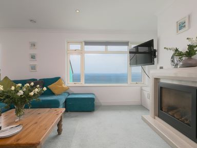 A living room with a turquoise sofa a wooden coffee table a fireplace a wall-mounted television and a large window with an ocean view at Moonbeams in Carbis Bay