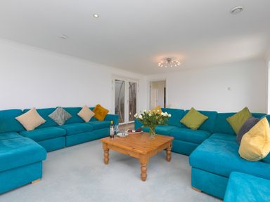 A living room with blue sofas and a wooden coffee table with flowers and wine at Moonbeams in Carbis Bay