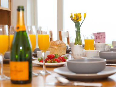 A dining table set with glasses of orange juice strawberries a loaf of bread and a vase with yellow flowers at Moonbeams in Carbis Bay