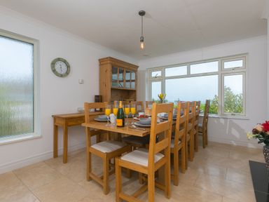 A dining room with a long wooden table set with plates and glasses and wooden chairs and a large window at Moonbeams in Carbis Bay