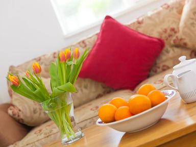 A living room with tulips in a glass vase oranges in a bowl and a teapot on a wooden table at Moonbeams in Carbis Bay