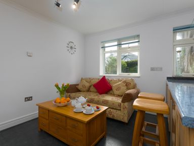 A sitting area with a floral sofa red pillow wooden coffee table with tea set and fruit bowl and wooden stools at Moonbeams in Carbis Bay