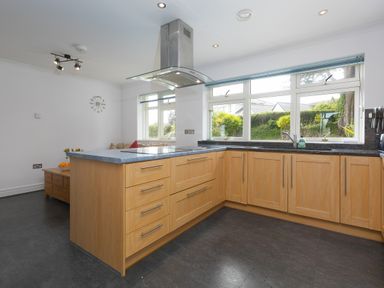 A kitchen with wooden cabinets a black countertop large windows and a stainless steel range hood at Moonbeams in Carbis Bay