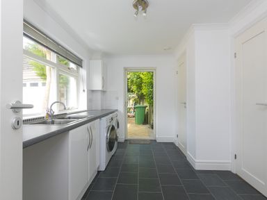 A utility room with a washing machine dryer and sink with a door leading outside at Moonbeams in Carbis Bay