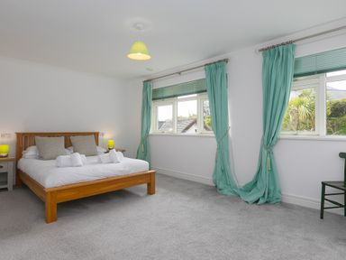 A bedroom with a wooden bed and side tables with lamps and windows with teal curtains at Moonbeams in Carbis Bay