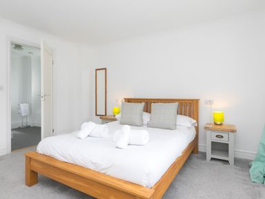 A bedroom with a wooden bed frame two bedside tables with lamps and a mirror on the wall at Moonbeams in Carbis Bay