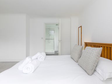 A bedroom with a double bed and rolled towels with an open door showing a shower at Moonbeams in Carbis Bay