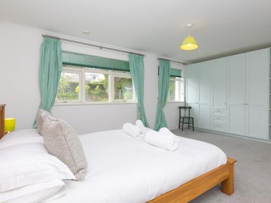 A bedroom with a wooden bed white bedding turquoise curtains green blinds large white wardrobe and a black chair at Moonbeams in Carbis Bay