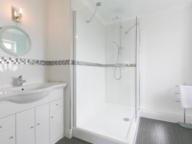 A bathroom with a sink vanity a round mirror a glass shower enclosure and a towel rack at Moonbeams in Carbis Bay