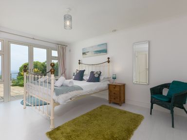 A bedroom with a metal bed frame pillows and rolled towels a wooden nightstand with lamps a green rug a chair and patio doors at Moonbeams in Carbis Bay