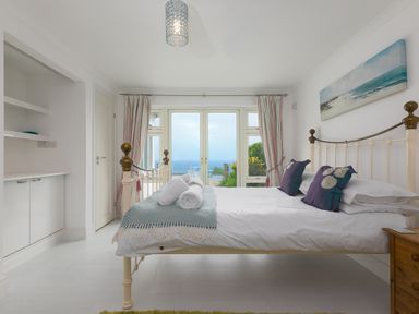 A bedroom with a bed facing glass doors showing a sea view at Moonbeams in Carbis Bay